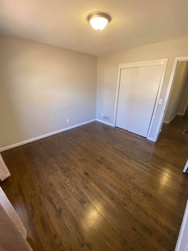 unfurnished bedroom with dark wood-type flooring, a closet, visible vents, and baseboards