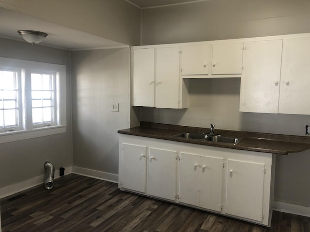 kitchen with dark wood-type flooring, dark countertops, a sink, and baseboards