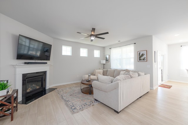 living room featuring ceiling fan, a glass covered fireplace, light wood-style flooring, and baseboards