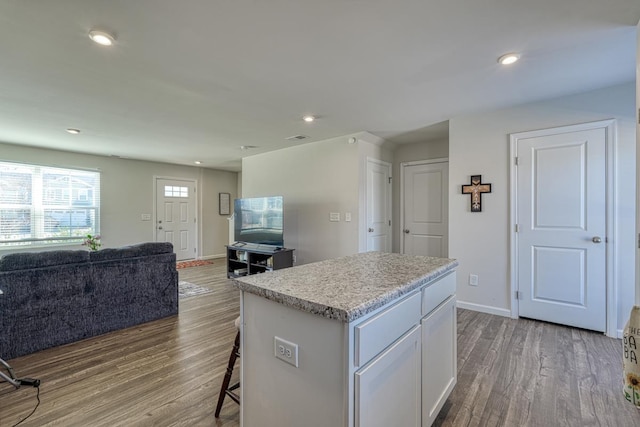 kitchen with open floor plan, wood finished floors, white cabinets, and a center island