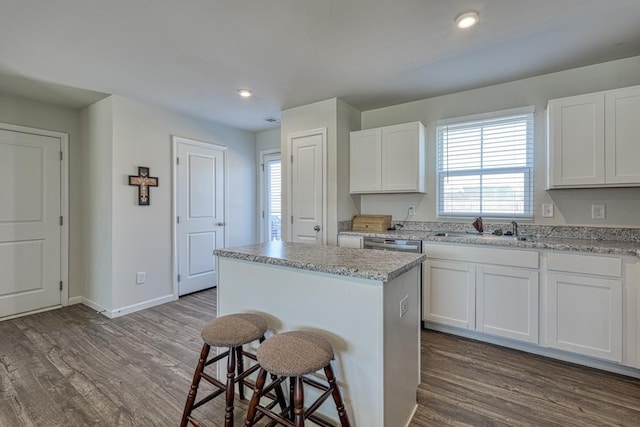 kitchen with a breakfast bar area, a sink, white cabinetry, a center island, and dark wood finished floors