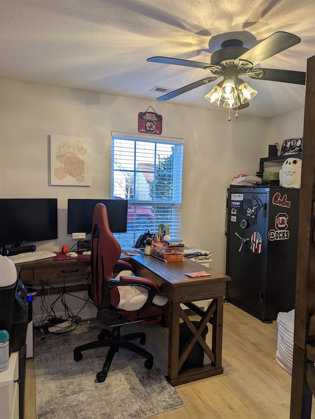 home office with light wood-style floors, ceiling fan, visible vents, and a textured ceiling