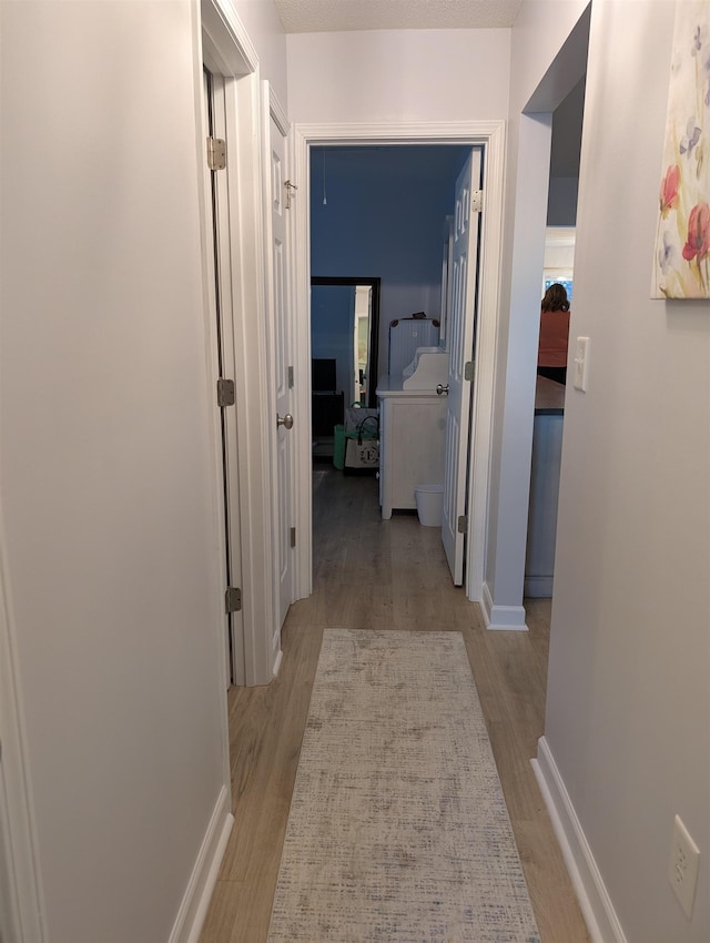 hall featuring light wood-style flooring and baseboards