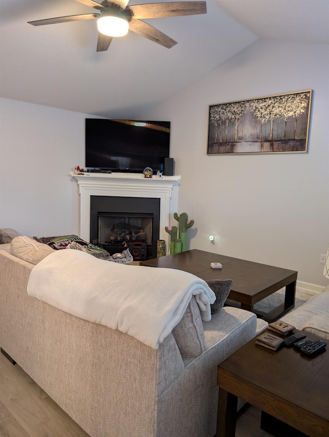 living area featuring vaulted ceiling, ceiling fan, a fireplace, and wood finished floors