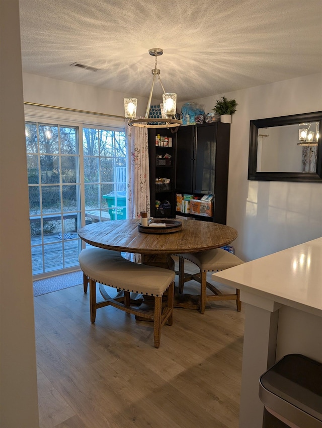 dining room with a textured ceiling, an inviting chandelier, and light wood-style floors