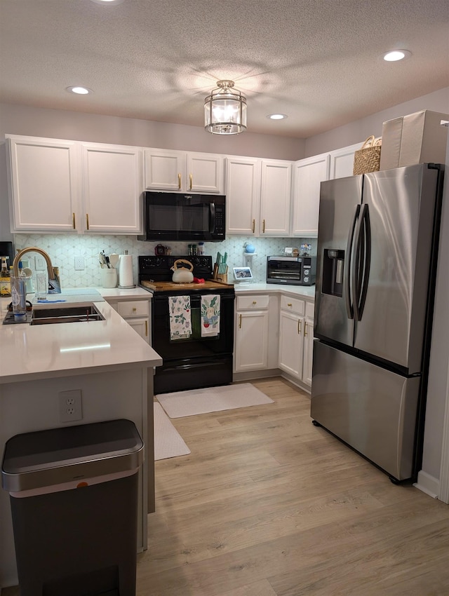 kitchen with decorative backsplash, white cabinets, light wood-type flooring, black appliances, and a sink