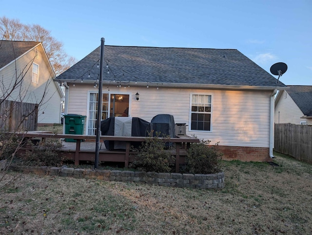 back of property with roof with shingles, fence, a deck, and a yard