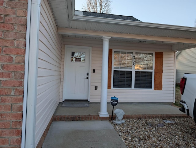 view of exterior entry with brick siding and a porch