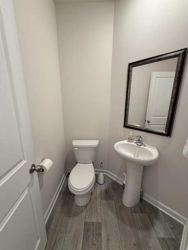 half bath featuring baseboards, toilet, and wood finished floors