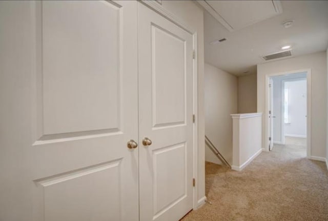 hall featuring attic access, visible vents, baseboards, light colored carpet, and an upstairs landing