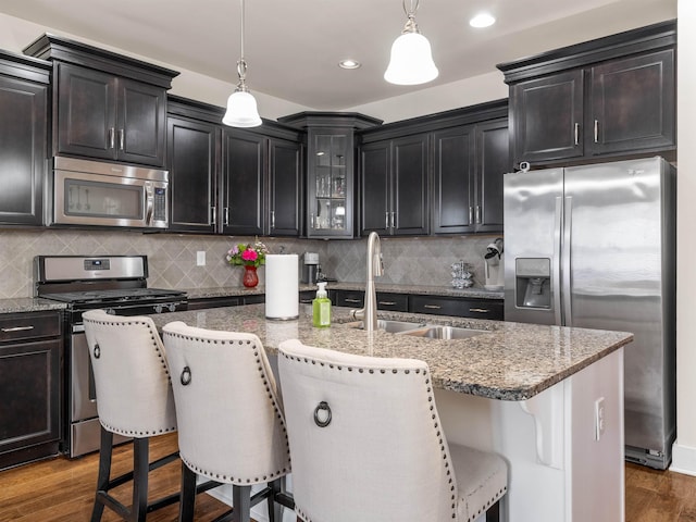 kitchen featuring dark wood-type flooring, a sink, appliances with stainless steel finishes, light stone countertops, and glass insert cabinets