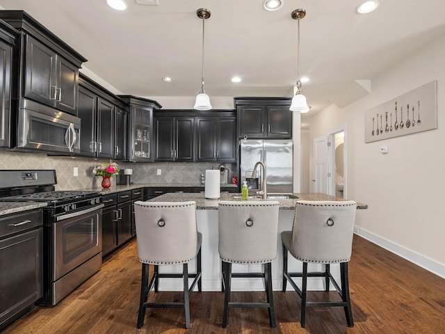 kitchen with a kitchen breakfast bar, dark wood-type flooring, a sink, stainless steel appliances, and backsplash