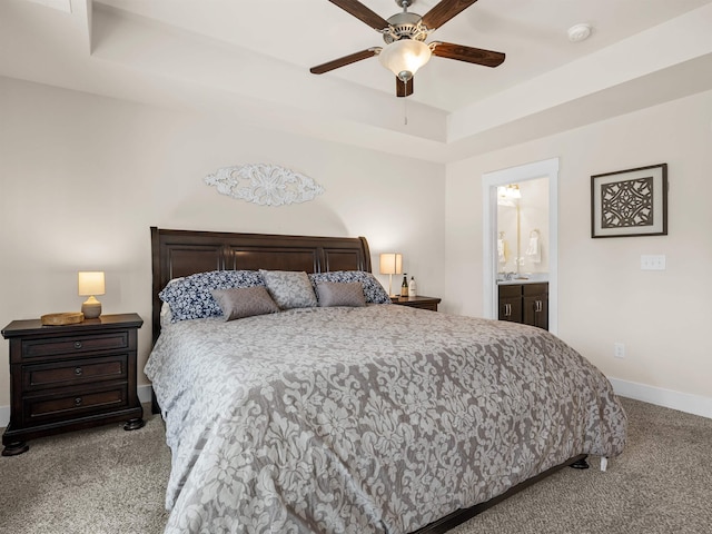 carpeted bedroom with a tray ceiling, ensuite bathroom, a sink, ceiling fan, and baseboards