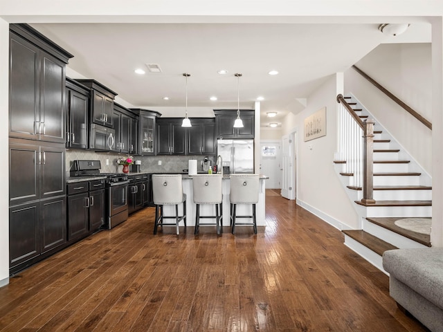 kitchen with a kitchen breakfast bar, hanging light fixtures, appliances with stainless steel finishes, decorative backsplash, and dark wood-style floors