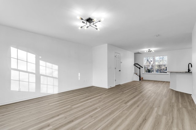 unfurnished living room featuring light wood-style flooring, a sink, stairway, and baseboards