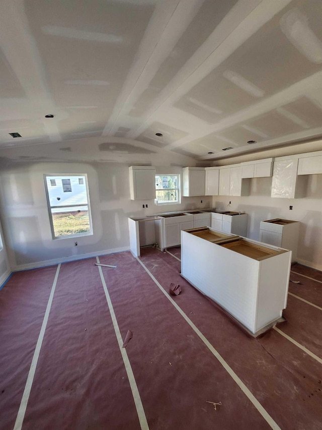 kitchen featuring lofted ceiling, a kitchen island, white cabinetry, and baseboards