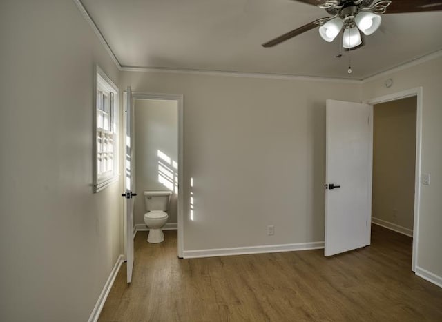 unfurnished bedroom featuring baseboards, ensuite bath, ceiling fan, wood finished floors, and crown molding