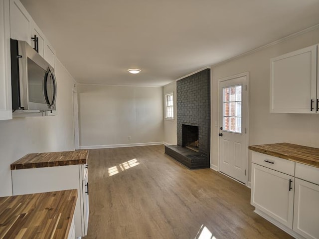 unfurnished living room with a brick fireplace, crown molding, baseboards, and wood finished floors