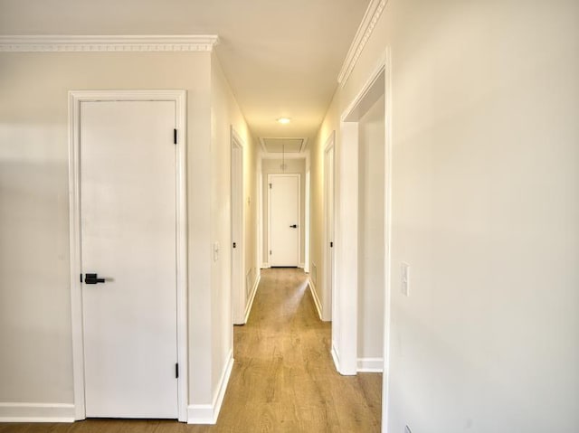 hallway with light wood finished floors, attic access, baseboards, and crown molding