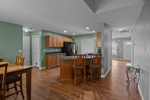 kitchen featuring dark wood-style flooring, visible vents, black fridge, dark countertops, and a kitchen bar