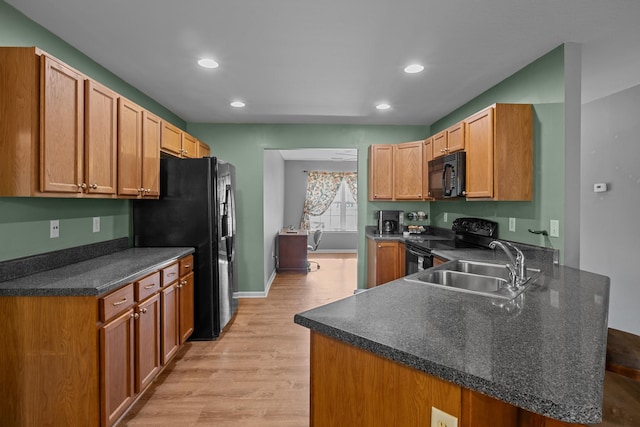 kitchen featuring dark countertops, light wood-style flooring, a sink, a peninsula, and black appliances