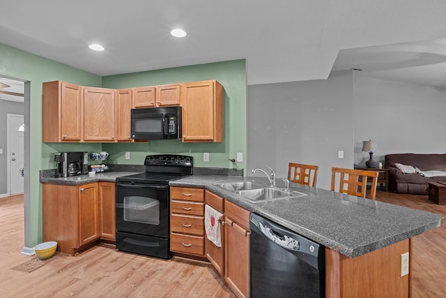 kitchen featuring a peninsula, a sink, black appliances, light wood finished floors, and dark countertops