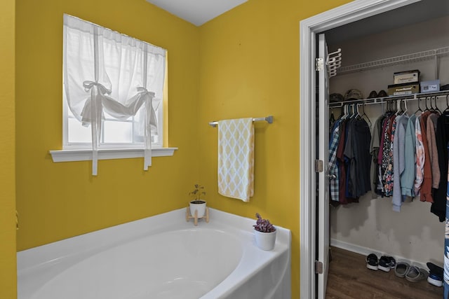 full bathroom with a garden tub, a spacious closet, baseboards, and wood finished floors