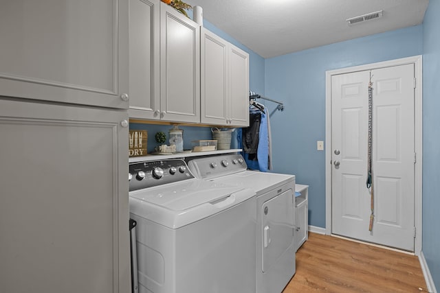 washroom featuring cabinet space, visible vents, a textured ceiling, light wood-type flooring, and washing machine and dryer