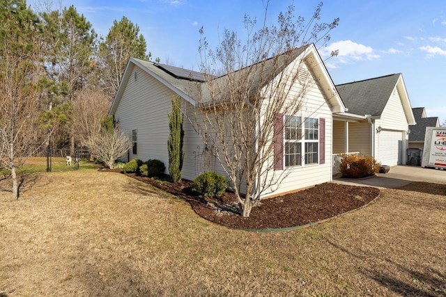 view of property exterior featuring an attached garage, solar panels, fence, driveway, and a lawn