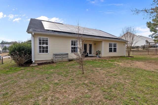 back of property with a yard, french doors, fence, and roof mounted solar panels