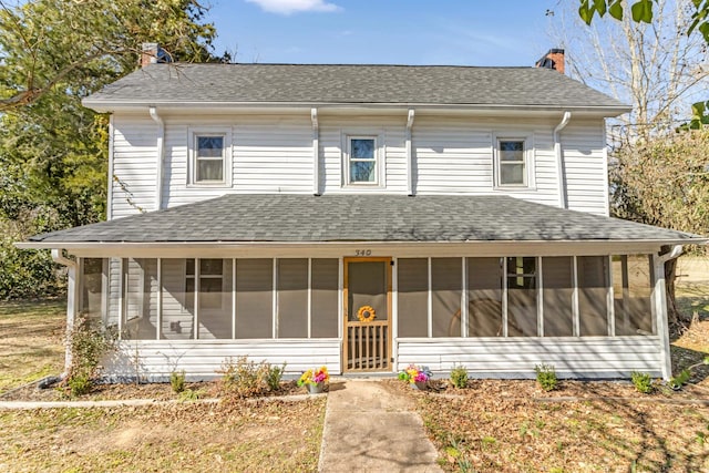 view of front facade with a sunroom, a shingled roof, and a chimney