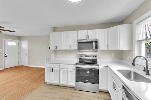 kitchen featuring light wood-style flooring, a sink, white cabinetry, light countertops, and appliances with stainless steel finishes