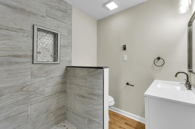 full bathroom with toilet, vanity, wood finished floors, tiled shower, and baseboards