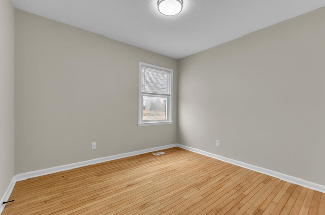 unfurnished room with baseboards, visible vents, and hardwood / wood-style floors