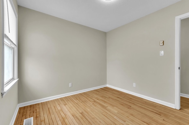 empty room with wood-type flooring, visible vents, and baseboards