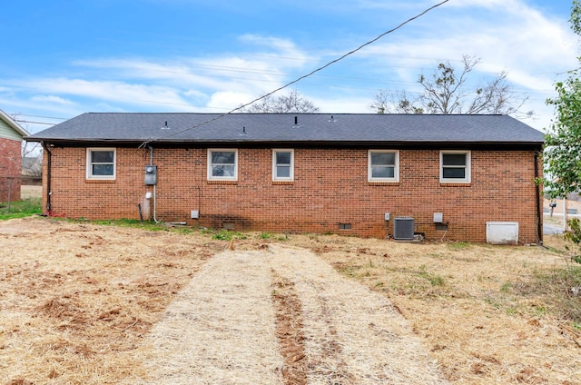 rear view of property with crawl space, brick siding, roof with shingles, and central AC unit