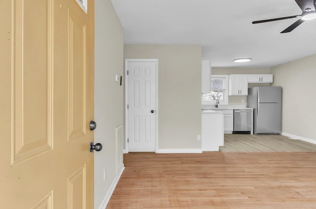 kitchen featuring light wood-style flooring, stainless steel appliances, baseboards, white cabinets, and light countertops