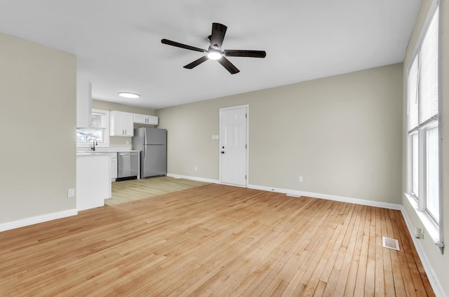 unfurnished living room with ceiling fan, light wood finished floors, visible vents, and baseboards