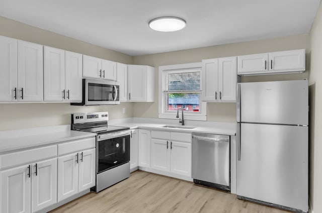 kitchen with light countertops, light wood-style flooring, appliances with stainless steel finishes, white cabinetry, and a sink