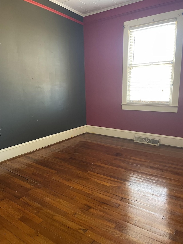 empty room featuring ornamental molding, wood-type flooring, visible vents, and baseboards