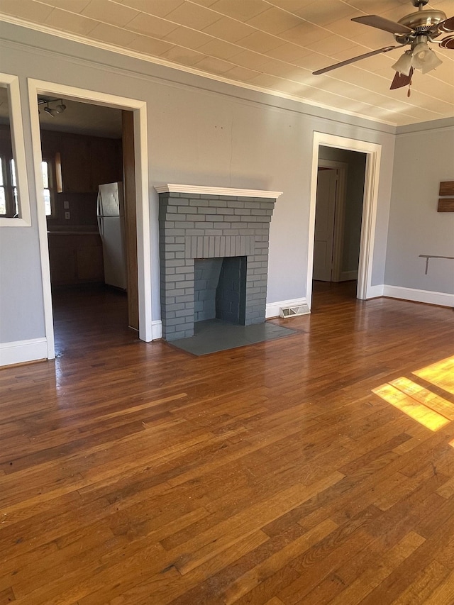 unfurnished living room featuring visible vents, a ceiling fan, a brick fireplace, wood finished floors, and baseboards