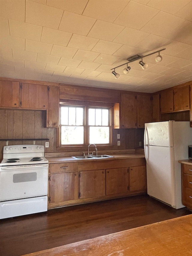 kitchen with dark wood-style flooring, brown cabinets, a sink, wooden walls, and white appliances