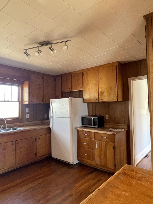 kitchen featuring stainless steel microwave, brown cabinets, dark wood-type flooring, freestanding refrigerator, and a sink