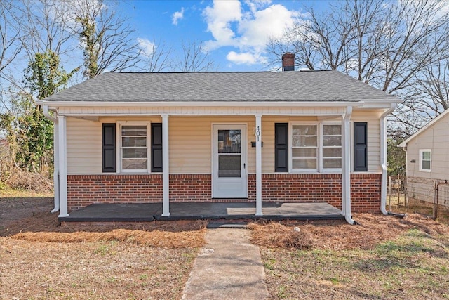 bungalow-style home with a chimney, a shingled roof, covered porch, and brick siding