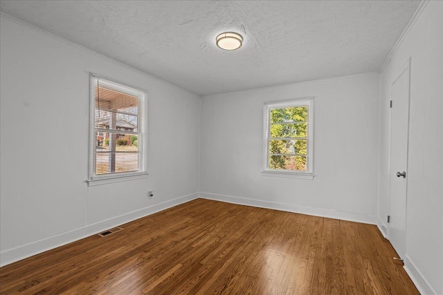 empty room with crown molding, wood finished floors, a textured ceiling, baseboards, and visible vents