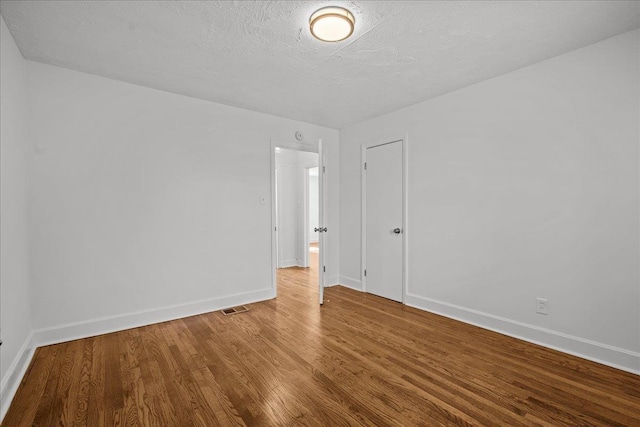 spare room featuring baseboards, visible vents, wood finished floors, and a textured ceiling