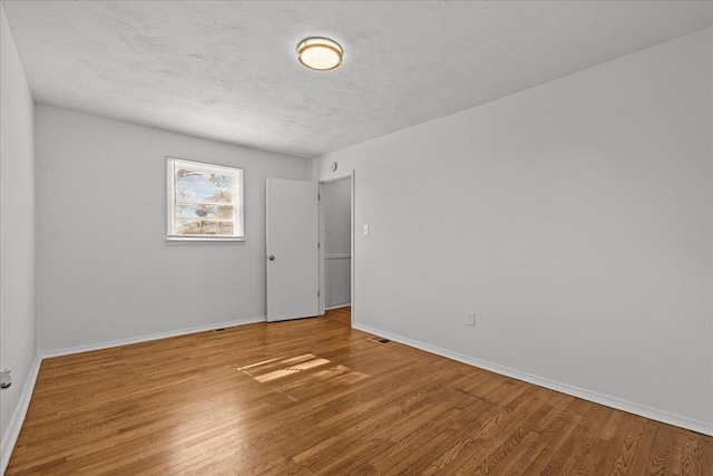 unfurnished room featuring visible vents, a textured ceiling, baseboards, and wood finished floors