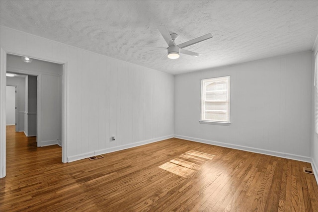unfurnished room featuring a textured ceiling, visible vents, wood finished floors, and a ceiling fan