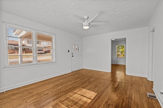 empty room featuring a textured ceiling, ceiling fan, visible vents, and wood finished floors