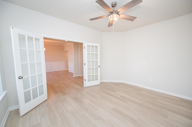 spare room with french doors, a wainscoted wall, a decorative wall, a ceiling fan, and light wood-type flooring